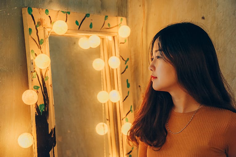 Profile of a woman beside a decorative lighted mirror indoors.